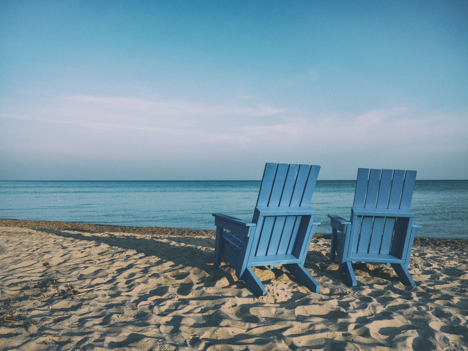 two blue adirondack chairs at a beach