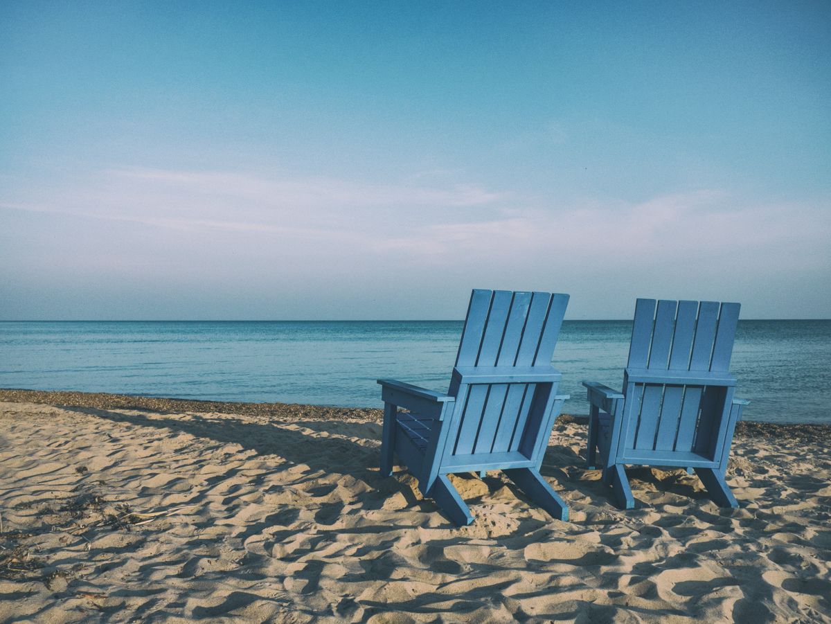 two blue adirondack chairs at a beach