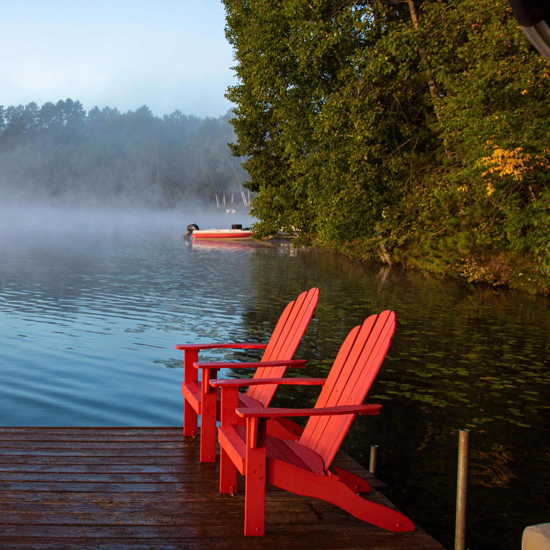 two red adirondack chairs on a dock with fog on the water 